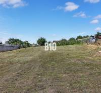 A flat residential plot in Rumanová, surrounded by greenery and neighboring fences.