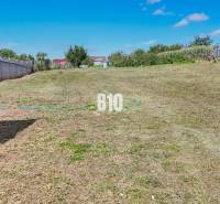A residential plot in Rumanová with a grassy surface, next to fences and houses.