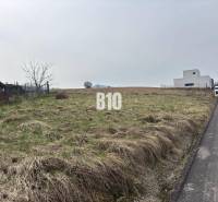 A plot for residential use in Rosina, next to the road, with a grassy surface and nearby buildings.