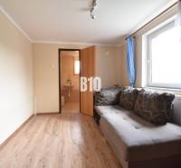 Living room in a family house with a sofa, a window with blue curtains, and a door to the bathroom.