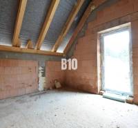 The ground floor of a family house showing raw brick walls and roof beams.