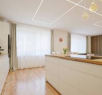 A kitchen in a family house with a wooden decor floor, light furniture, and a large window.