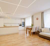 Interior of a family house with a kitchen and living room, wooden decor flooring, and light-colored furniture.