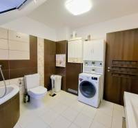 A bathroom in a 3-room apartment with a corner bathtub, a washing machine, and light tiles.