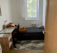 A small room in a 3-room apartment with a wooden decor floor, bed, table, chair.