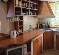 A kitchen in a family house with wooden cabinets and shelves, complemented by a wall clock.