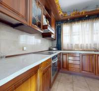 A kitchen in a 5 or more room apartment with wooden cabinets and light curtains.