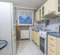 A kitchen in a 3-room apartment with white tiles, appliances, and a table.