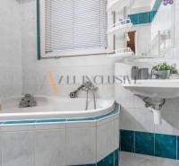 A bathroom with white and blue tiles, a corner bathtub, and a sink in a 3-room apartment.