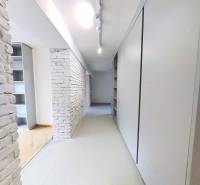 A narrow hallway in a 2-room apartment with white brick walls and cabinets.