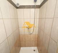 Tiled shower corner in a 2-room apartment with a simple design and a showerhead.