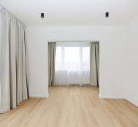 A room in a 3-room apartment with a wooden decor floor and large windows with curtains.