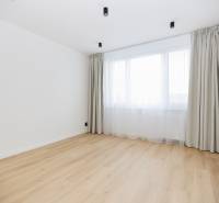 An empty room with a window, curtains, and a wooden-patterned floor in a three-room apartment.