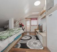 Attic room in a family house with a bed, TV, decorations, and a floor with a wooden decor.