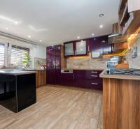 A kitchen in a family house with glossy purple cabinets and a wooden-patterned floor.