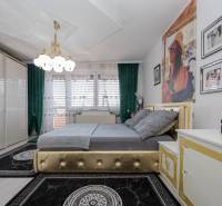 Bedroom in a family house with a bed, green curtains, and gold details on the furniture.