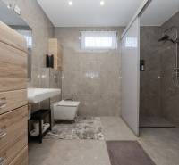Bathroom of a family house with tiles and a shower corner, cabinets with wooden decor.