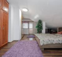 A bedroom in a family house with a bed, wardrobe, and wooden decor flooring.