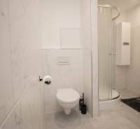 A bathroom with a shower, toilet, and white tiles in a 3-room apartment.