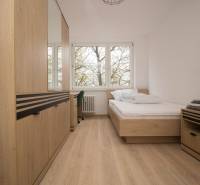 Bright bedroom in a three-room apartment with wood-patterned flooring and large windows.