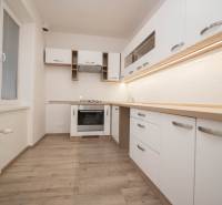 A kitchen with appliances, white cabinets, and a wood-patterned floor in a two-room apartment.