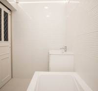 Bathroom in a 2-room apartment with white tiles, a sink, and a bathtub.