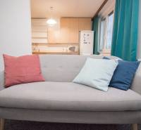 A gray sofa with colorful cushions in a 4-room apartment by the window and the kitchen.