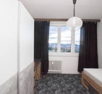 A room in a 4-room apartment with a bed, dark curtains, and a view from the window.
