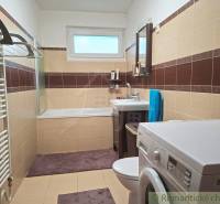 Bathroom in a family house with a bathtub, washing machine, and brown-beige tiles.