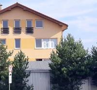 Yellow house with a sloped roof and windows behind trees near the office lines.