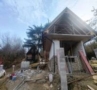 A cottage construction on Zajačia debra in Holčíkovce surrounded by trees and building materials.