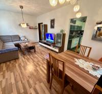 Living room in a three-room apartment with a wooden decor floor, a sofa, and a television.