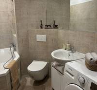 Bathroom in a 2-room apartment with a bathtub, washing machine, and soft beige tiles.