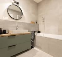 Bathroom in a 2-room apartment with a bathtub, sink, and a round mirror on the wall.