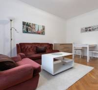 Living room of a two-room apartment with a burgundy sofa, white table on a floor with a wooden decor.