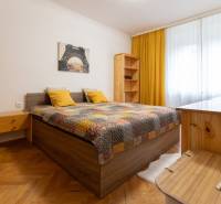 A bright bedroom in a two-room apartment with a bed, yellow pillows, and a wooden decor floor.