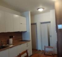 A kitchen in a 2-room apartment with a wooden decor floor and white cabinets.