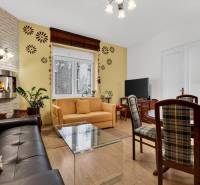 A bright living room with a fireplace, sofa, TV, and wood-patterned flooring in a three-room apartment.