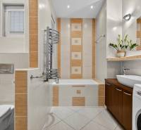 A bathroom with a bathtub, washing machine, sink, and decorative tiles in a 3-room apartment.