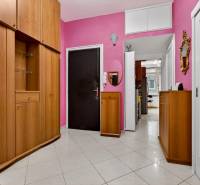 A spacious hallway of a 3-room apartment with wooden cabinets and pink walls.