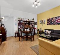 Living room with wood-patterned flooring, paintings, a dark brown couch, and a dining table.
