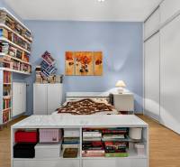 A bedroom with wood-patterned flooring, shelves full of books, and white furniture.