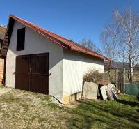 A cottage in Zlaté Moravce with wooden doors and a sloped roof in the yard.
