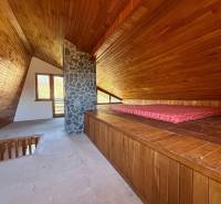 The attic of the cottage with wooden decor and a stone chimney resembles a cozy relaxation space.