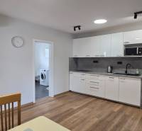 A kitchen with white cabinets and appliances in a 3-room apartment, with a wood-patterned floor.