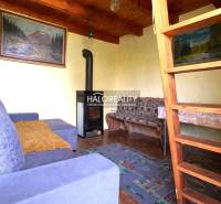 The interior of a cabin with a fireplace, wooden ceilings, and stairs to the attic.