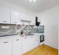 A kitchen in a one-room apartment with white furniture and a wooden decor floor.