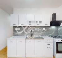 A kitchen with white cabinets in a studio apartment, a branded stove, and a floor with a wooden decor.