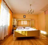 A bedroom in a family house with a double bed, orange curtains, and a wooden-patterned floor.