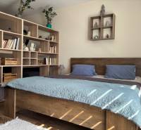 A bedroom in a one-room apartment with wooden furniture, a bed, and a shelving system.